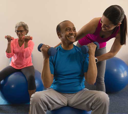 Couple with fitness trainer sitting on exercise balls with weights in hands