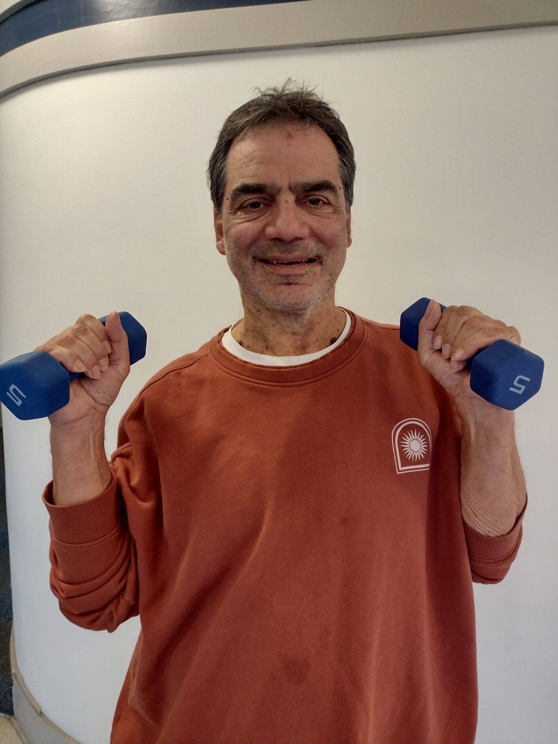Leo is a personal trainer for seniors in Seattle and is shown holding 2 dumbbells and smiling.
