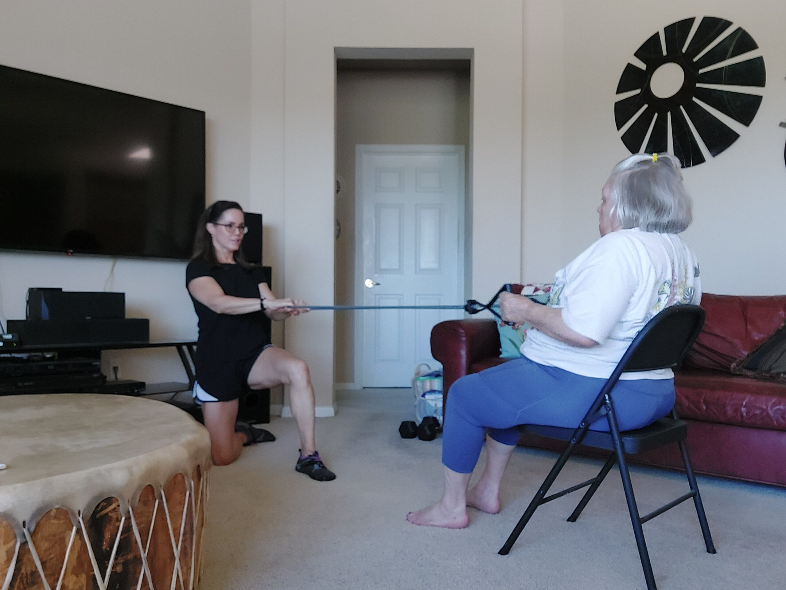 Picture of Paige a personal trainer for seniors in Austin helping a customer with a seated exercise for her back using a band.