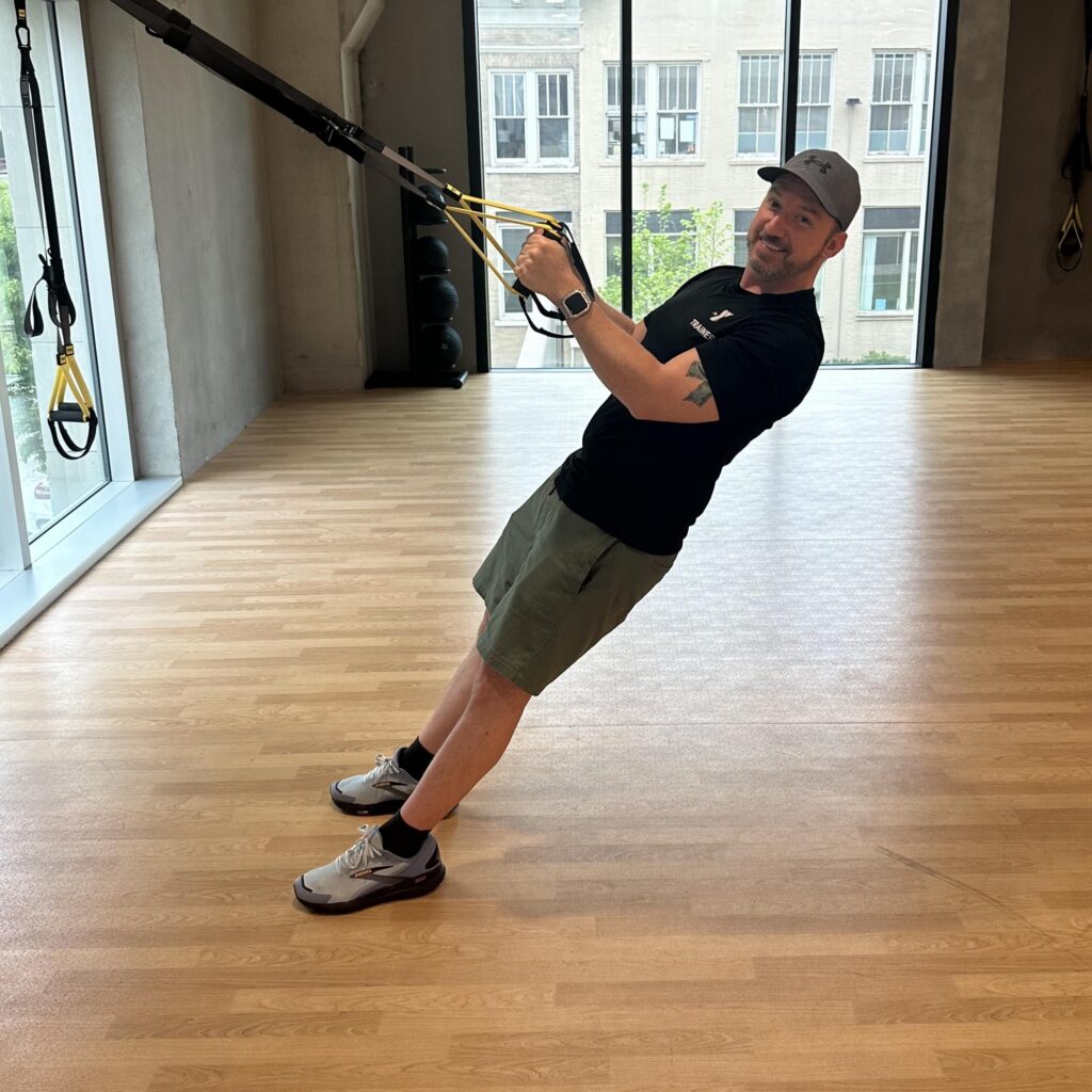 Picture of a smiling Brandon, a top personal trainer for seniors in Kansas City holding himself up using bands in a gym