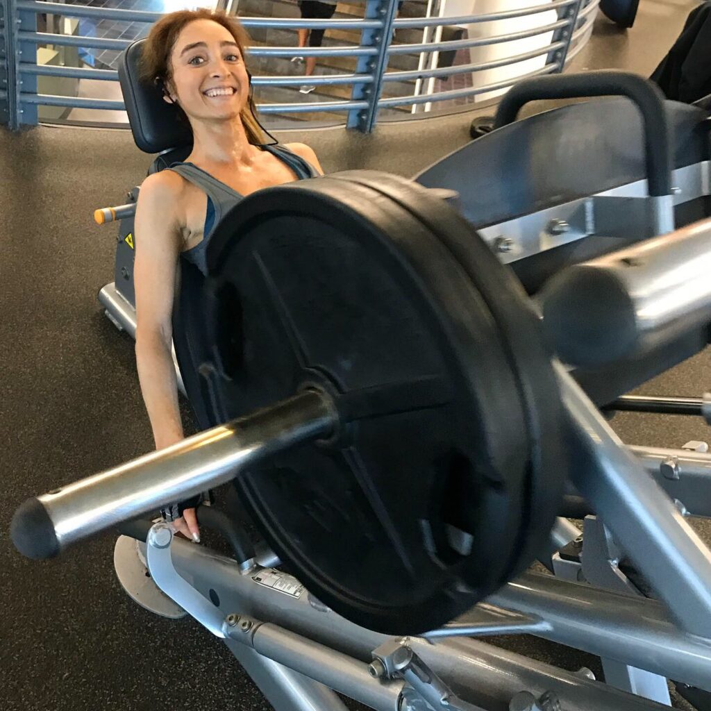 Picture of Nicole an ElderFIT personal trainer for seniors in Hollywood and Studio City smiling at camera and using a leg press machine to workout.